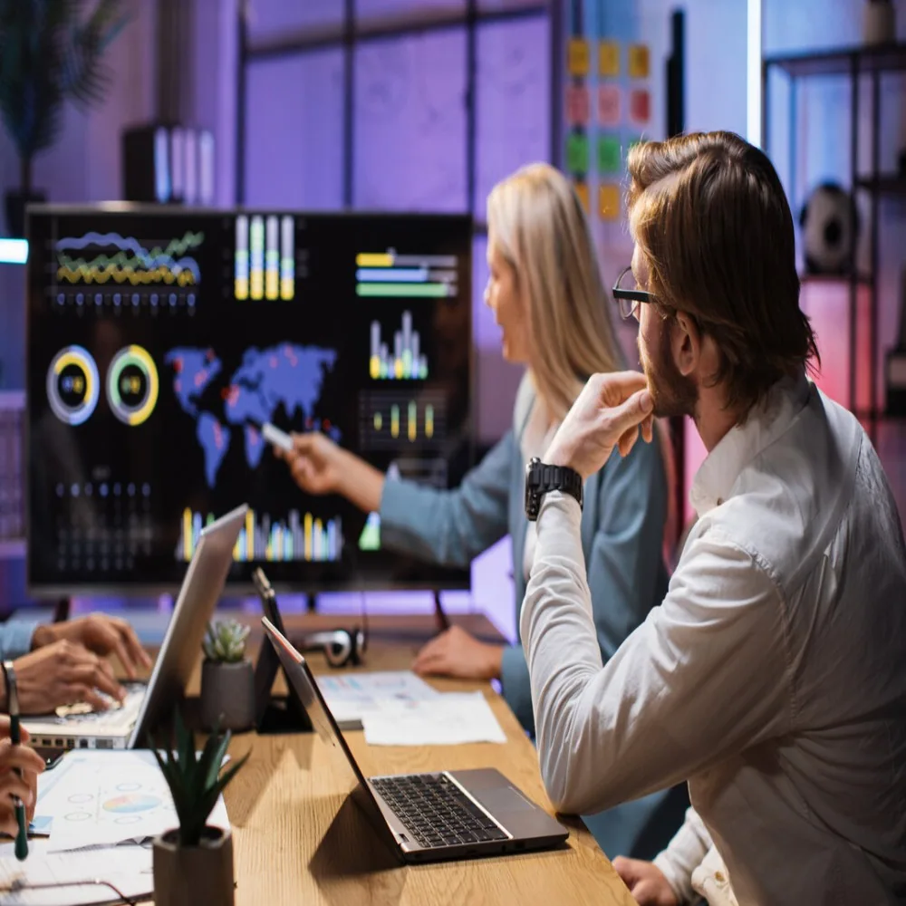 Team analyzing global business data on a monitor, using data-driven insights for strategic decision-making.