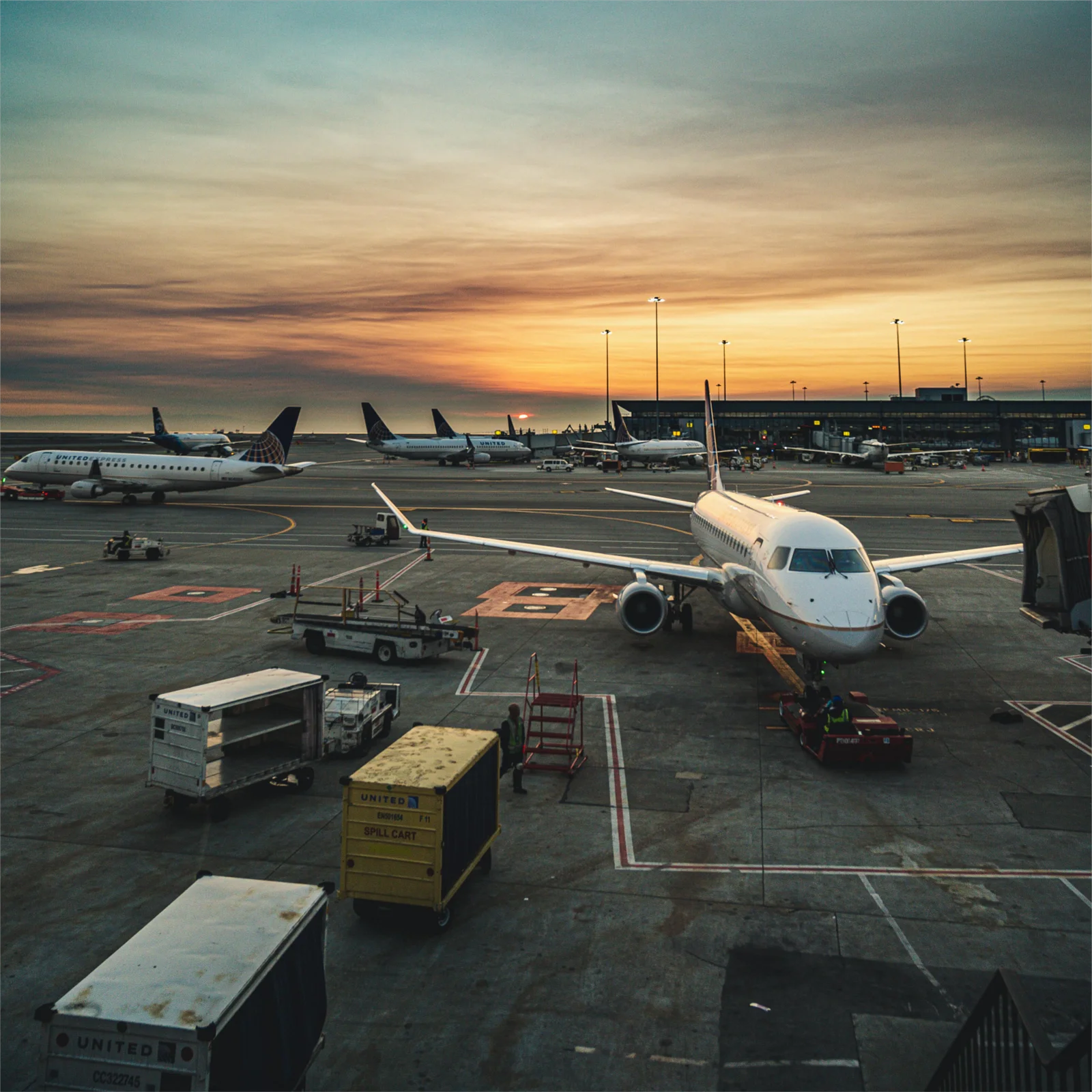 Airport tarmac at sunset with multiple United Airlines planes, ground support equipment.